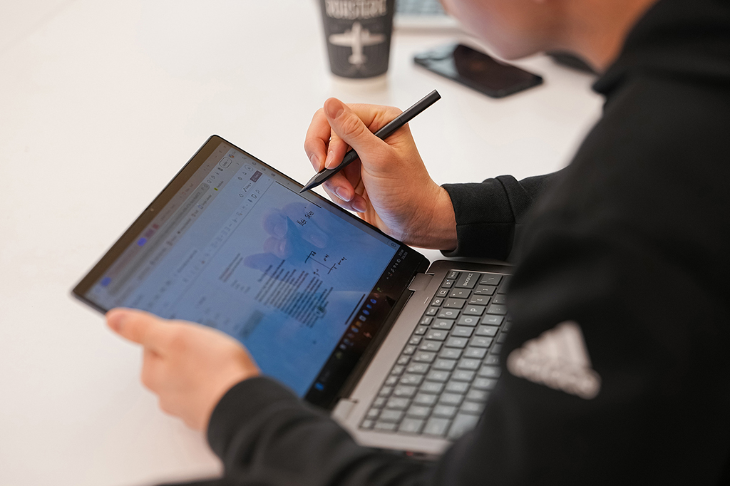 A close-up view of a student using a stylus to write notes on a touchscreen laptop during an accounting class.
