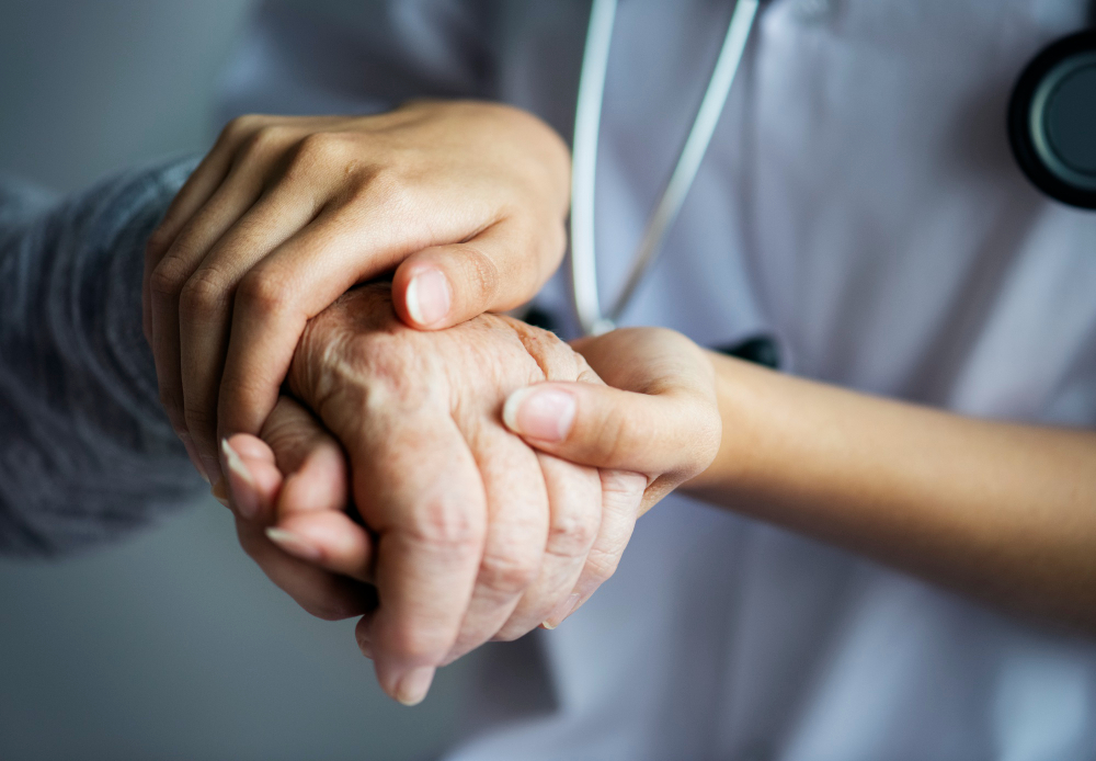 Close-up of a healthcare provider in scrubs gently holding an elderly patient's hand.