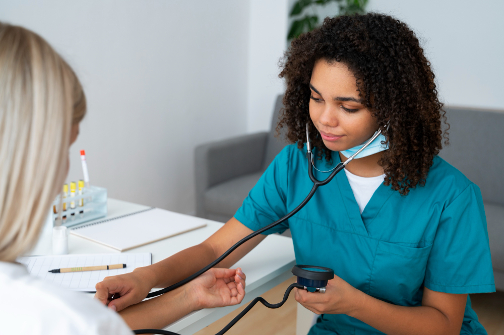 A nurse in teal scrubs wearing a stethoscope while taking a patient's blood pressure.