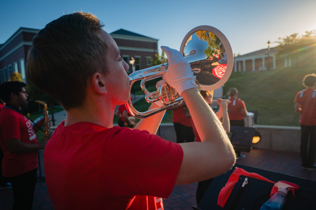 Close-up of a student playing a silver trumpet while wearing white gloves and a red shirt during a Cardinal Sound marching band performance.