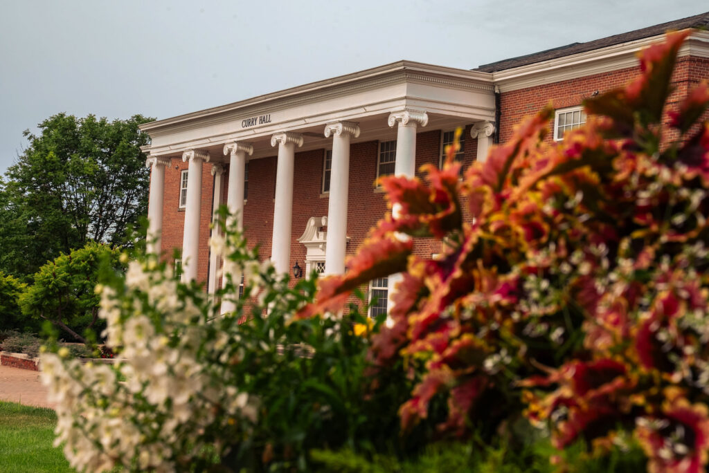 Exterior view of Curry Hall’s white columns and brick facade at William Jewell College framed by colorful flowers.