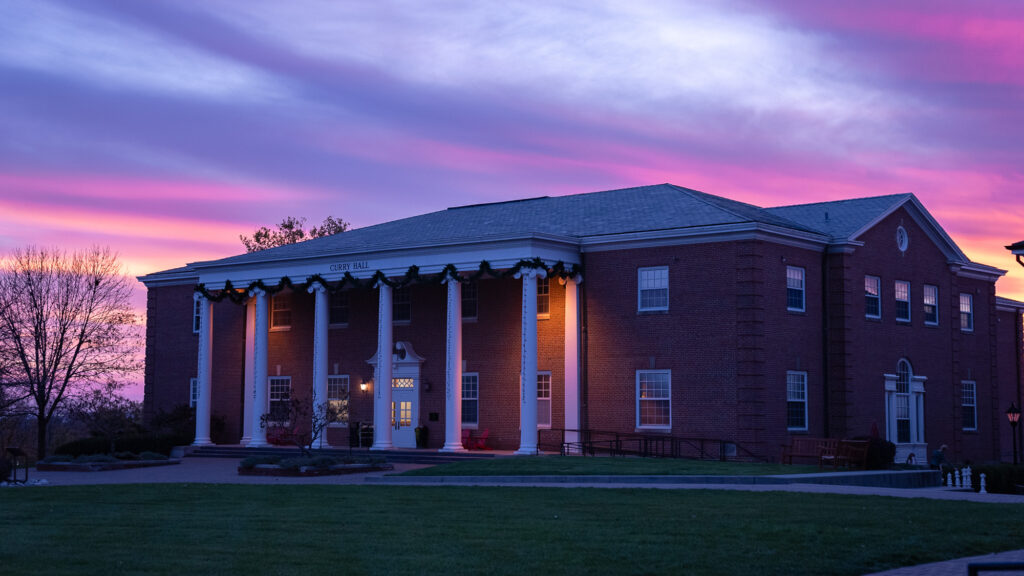 Exterior front view of Curry Hall illuminated against a vibrant pink and purple sunset sky.