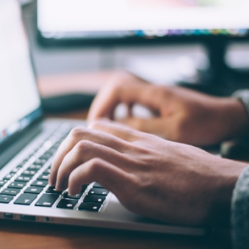 Close-up of hands typing on a laptop keyboard at a desk.