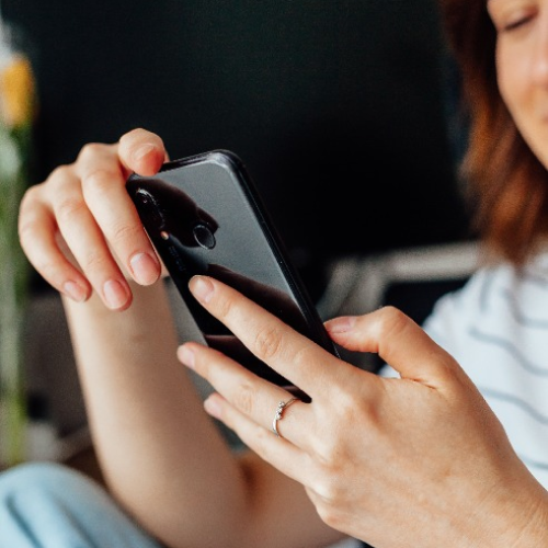 Close-up of a person holding a black smartphone while typing with their thumb.
