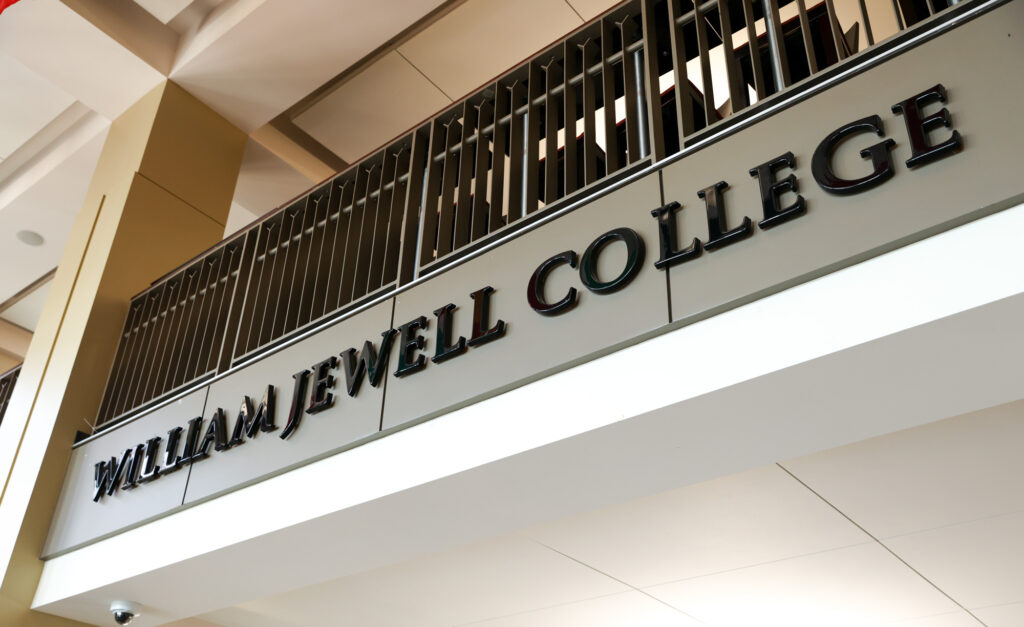 Low-angle view of interior architectural signage displaying raised black lettering that reads "WILLIAM JEWELL COLLEGE" below a second-floor balcony railing.