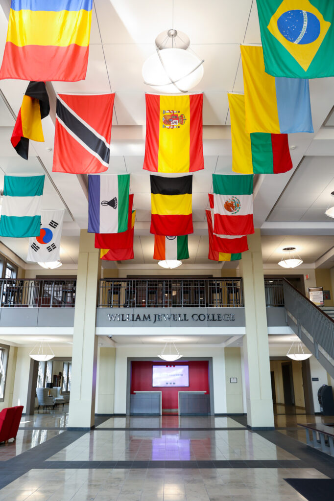 Interior atrium of Yates Gill College Center decorated with international flags hanging from the ceiling above the central lobby area.