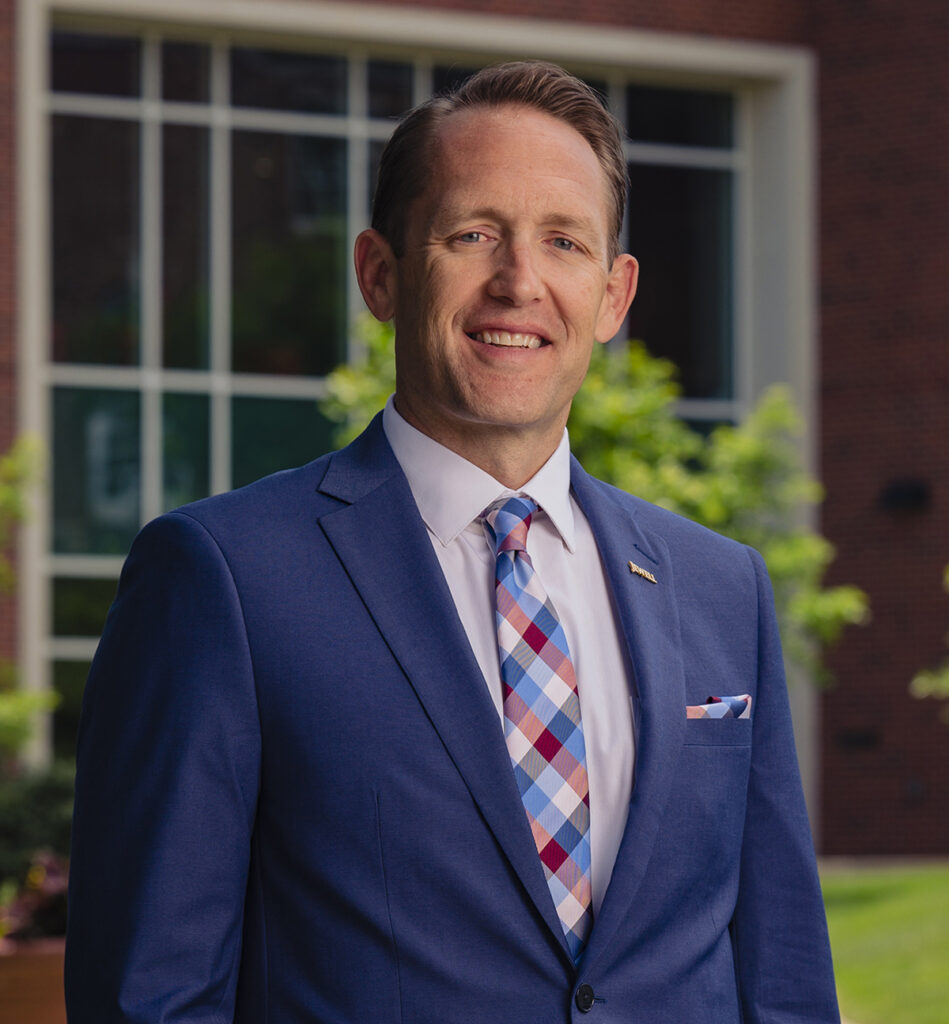 Headshot of Eric Blair, Vice President for Marketing, Enrollment, and Student Life at William Jewell College, wearing a blue suit and checkered tie.