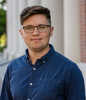 Headshot of Conon Gillis, Head Esports Coach at William Jewell College, wearing glasses and a patterned blue button-down shirt.