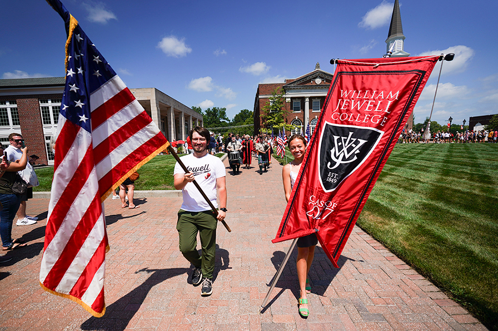 Students carrying an American flag and a William Jewell College Class banner while leading a procession across the campus quad.