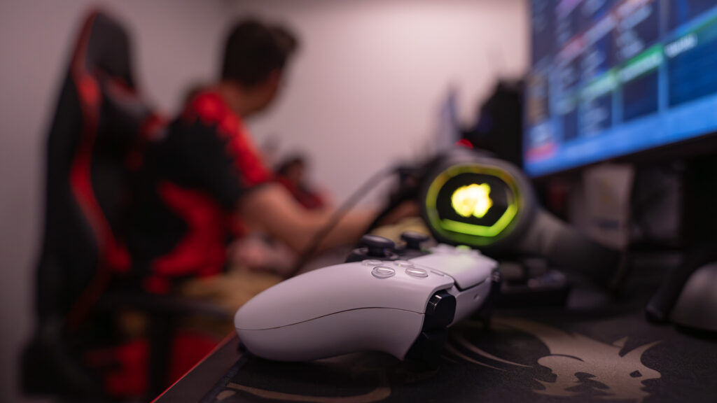Close-up of a white gaming controller resting on a desk with a gaming headset in an esports room.