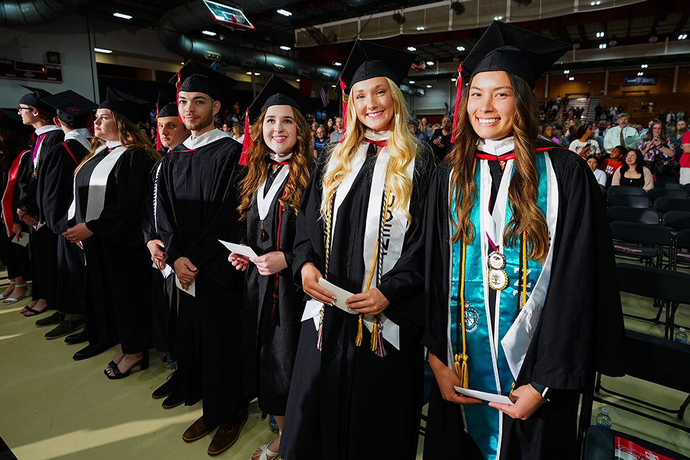 Graduating students in academic regalia smiling while standing in line inside the Mabee Center during commencement.