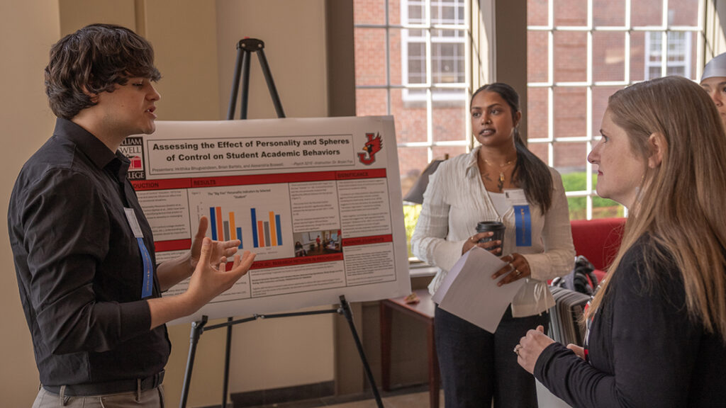 A student presenting a psychology research poster titled "Assessing the Effect of Personality and Spheres of Control on Student Academic Behaviors" to attendees.