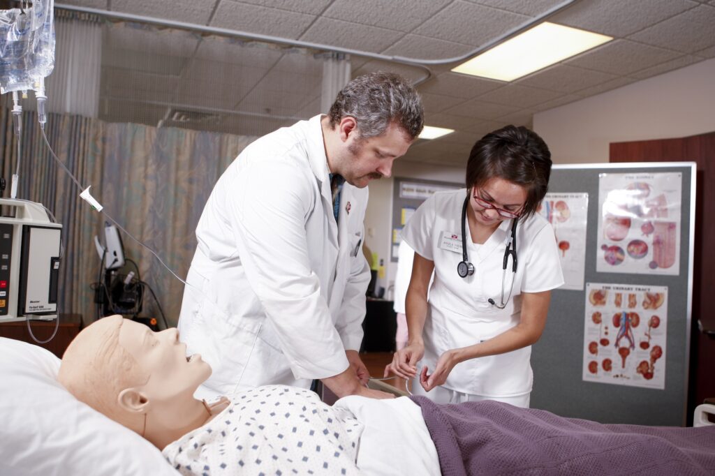 An instructor guiding a nursing student as she practices clinical care on a medical mannequin.
