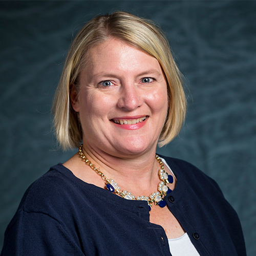 Headshot of Dr. Annette Behney, Associate Professor of Nursing at William Jewell College, wearing a navy cardigan and statement necklace against a gray backdrop.