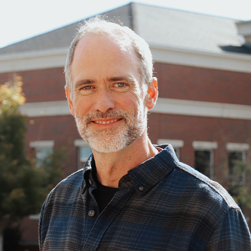 Headshot of Dr. Brendon Benz, Professor of History and Theologian-in-Residence at William Jewell College, wearing a plaid button-down shirt outdoors in front of a campus building.