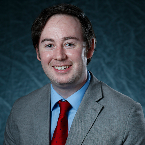 Headshot of Chris McCullick, Division Chair for Business, Communication, and Education and Professor of Accounting at William Jewell College, wearing a gray suit jacket, light blue shirt, and red tie against a gray backdrop.
