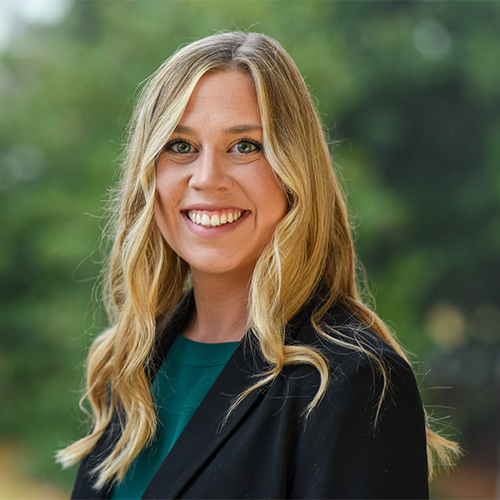 Headshot of Dr. Abigail Vegter, Assistant Professor of Political Science at William Jewell College, wearing a black blazer and green top against a green outdoor background.