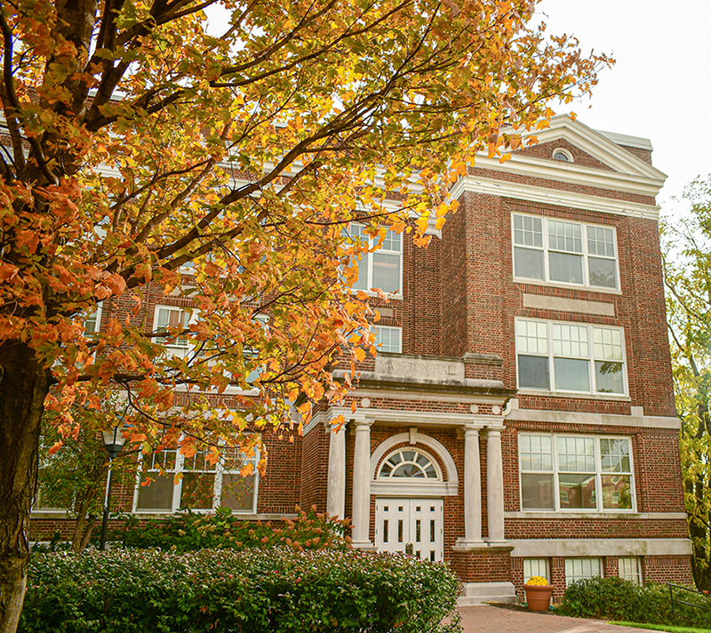 The exterior entrance of brick Marston Hall partially framed by autumn leaves on a tree.