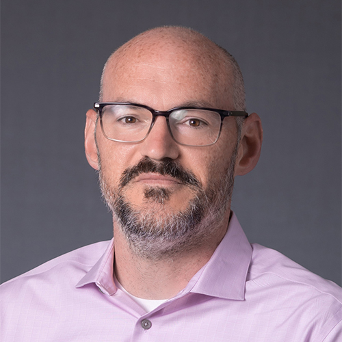 Headshot of Dr. Jared Bartels, Associate Professor of Psychological Science at William Jewell College, wearing glasses, a short beard, and a light pink button-down shirt against a gray backdrop.