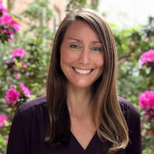 Headshot of Dr. Megan Groninger, Assistant Professor of History at William Jewell College, smiling in front of pink flowering bushes.