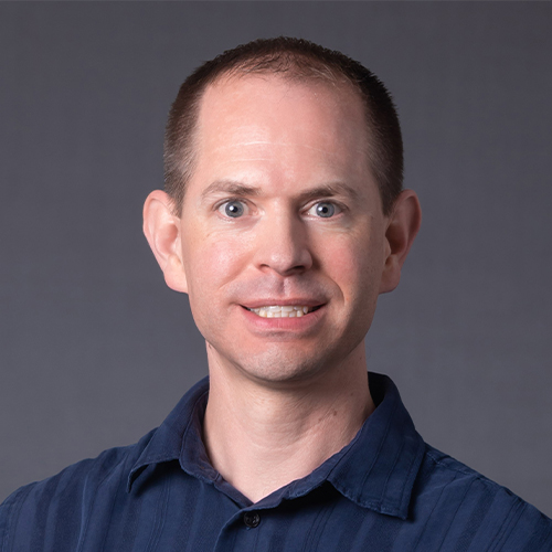 Headshot of Dr. Shane Price, Associate Professor of Chemistry at William Jewell College, wearing a dark blue button-down shirt against a gray backdrop.