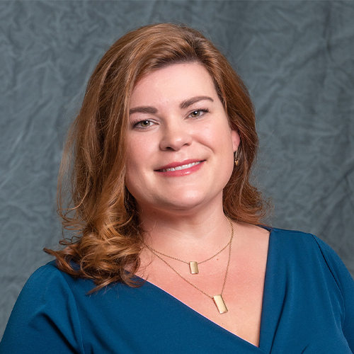 Headshot of Patty Richter, Assistant Professor of Nursing at William Jewell College, with shoulder-length reddish-brown hair, wearing a teal top and gold layered necklace against a gray backdrop.