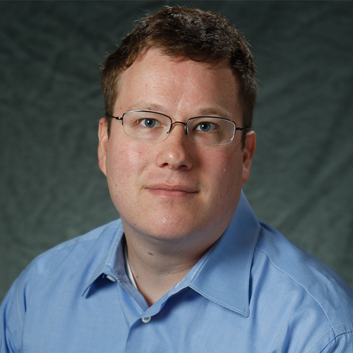 Headshot of Dr. Michael Stoll, Associate Professor of Education at William Jewell College, wearing glasses and a light blue button-down shirt against a gray backdrop.