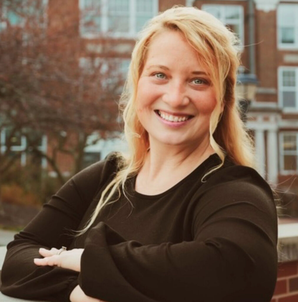 Tiffany Condren, Interim Nursing Program Director and Assistant Professor of Nursing, smiling with arms crossed in front of a brick campus building.