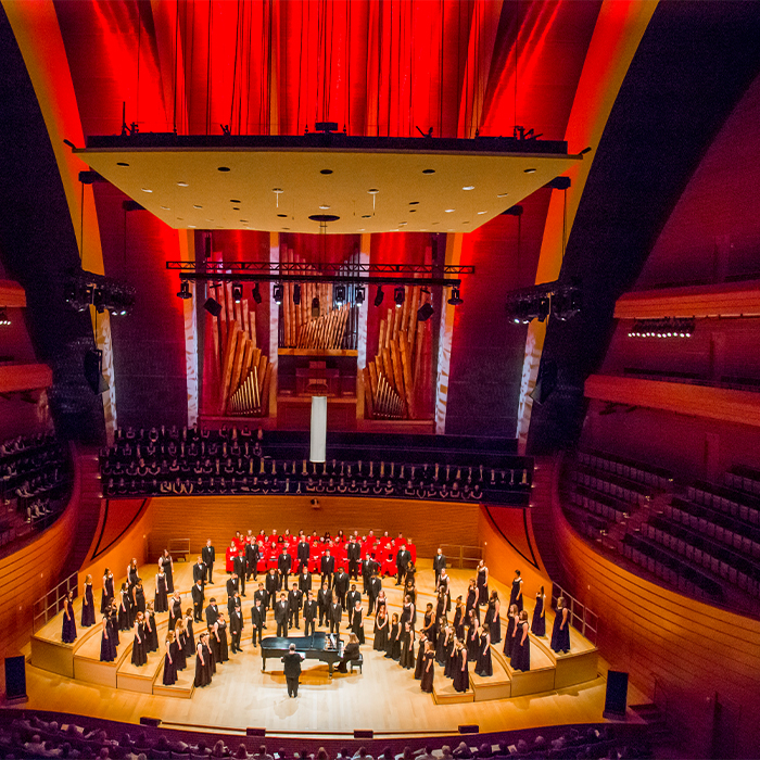 The William Jewell College choir performing on stage inside the Kauffman Center for the Performing Arts under red stage lighting.