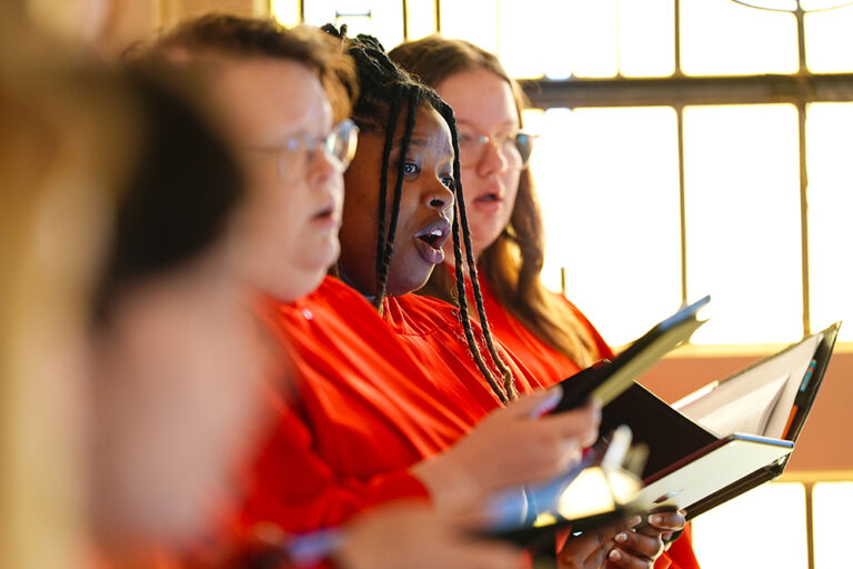 Close-up view of Concert Choir members singing together in red robes while holding black folders.