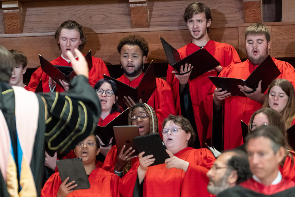 Members of the Concert Choir singing in red robes under the direction of a conductor during a performance.