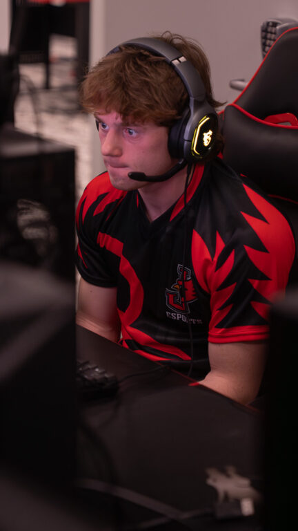 An Esports Overwatch team player wearing a headset and team jersey focused intently on a computer monitor.