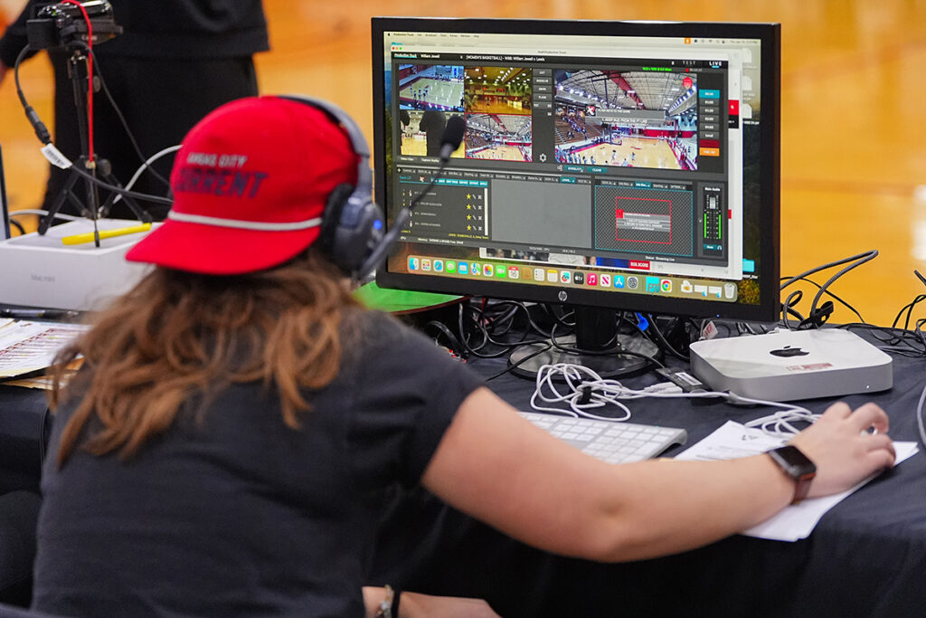 A student wearing headphones and a red Kansas City Current hat operating a live video broadcast interface on a desktop computer.