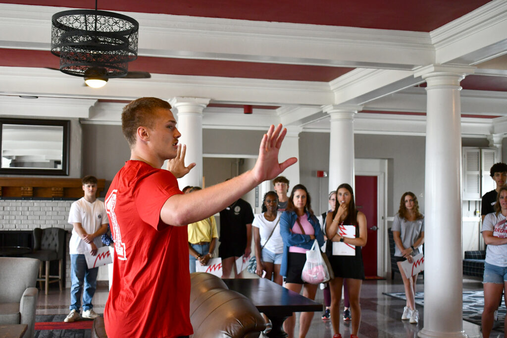 A tour guide gesturing with his hands while addressing a group of prospective students and families in a lounge area.