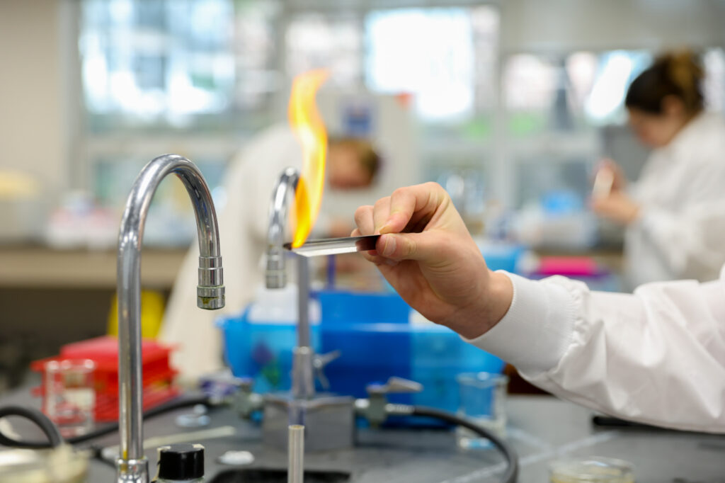Close-up view of a student holding a metal strip over an open flame during a laboratory experiment.