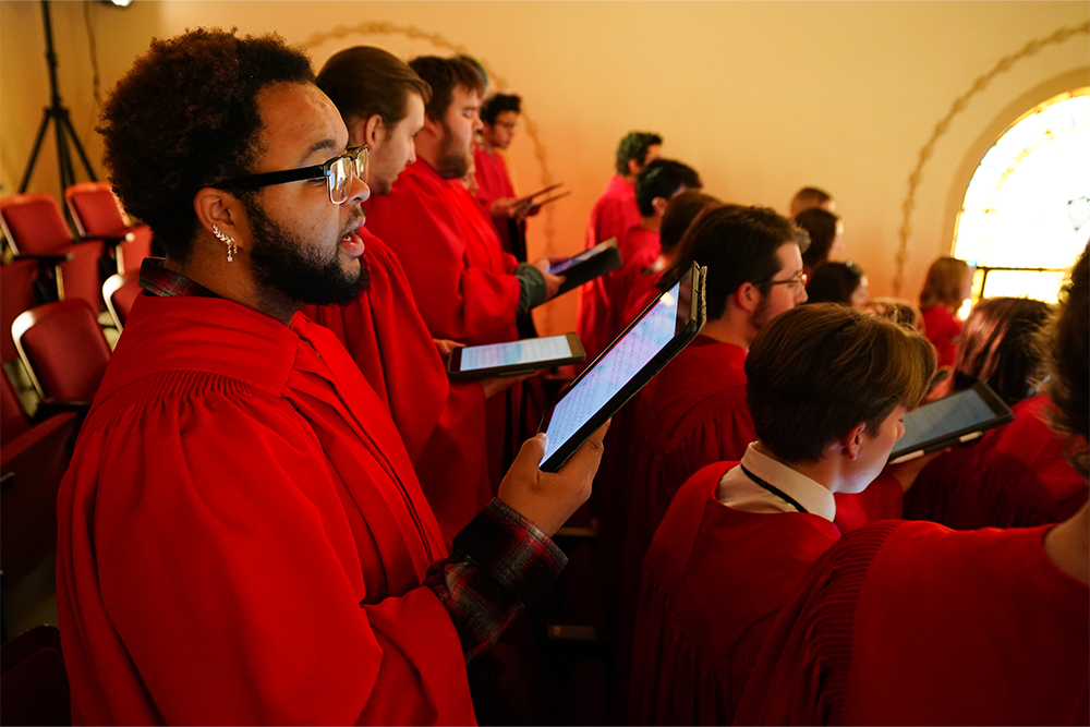 Members of the William Jewell Concert Choir wearing red robes and reading music off digital tablets inside Gano Chapel.