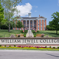 The William Jewell College entrance sign with flowerbeds, stairs, and Jewell Hall on the hill behind it.