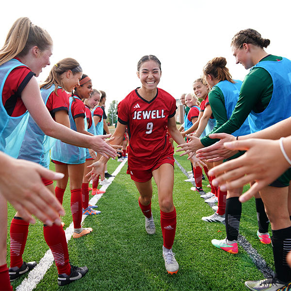 A William Jewell women's soccer player running down a line of high-fiving teammates during pregame introductions.