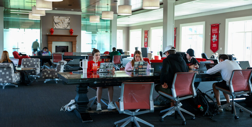 Students working on laptops at a long shared table inside Pryor Learning Commons.