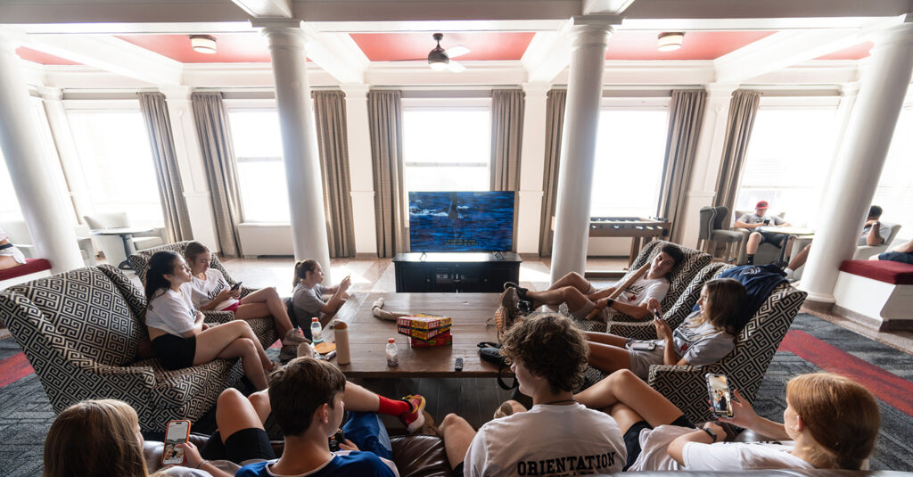 A group of students relaxing and looking at their phones in a residence hall lounge area.