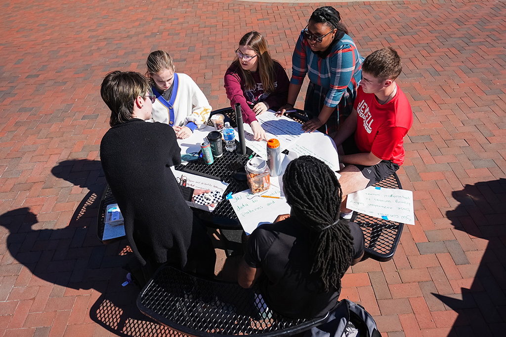 A group of students working together at an outdoor table with giant notepad sheets during an education class.