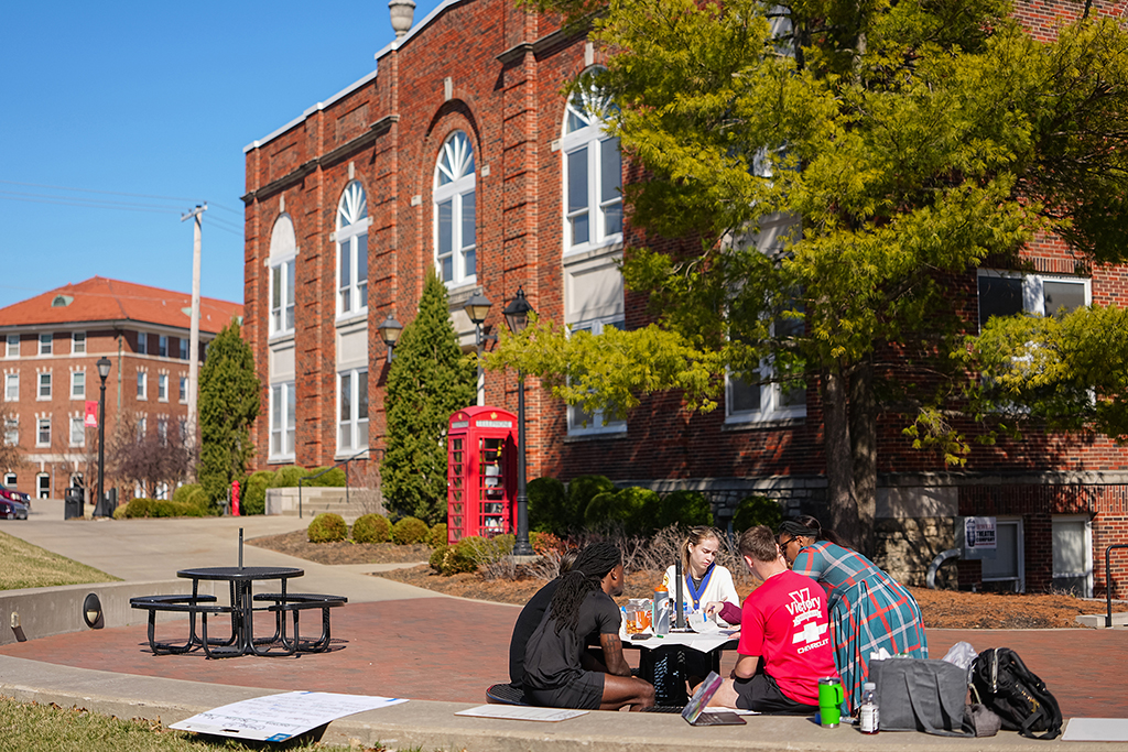 Students seated around a patio table studying outside Yates-Gill College Union near the iconic red phone booth.