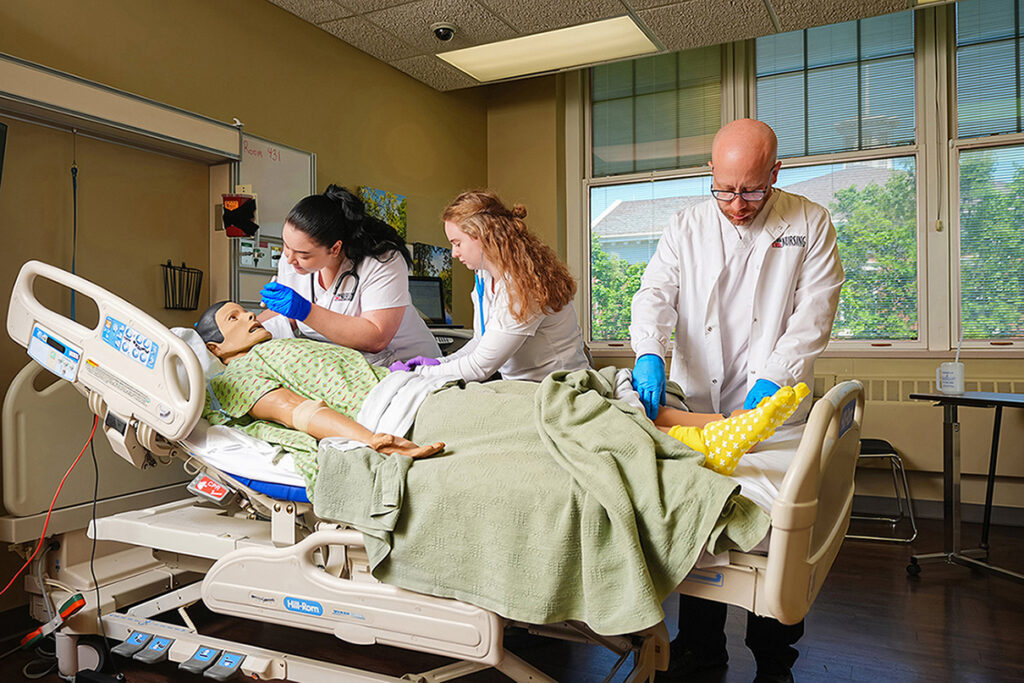 3 nursing students in lab, working on manikin patient in hospital bed