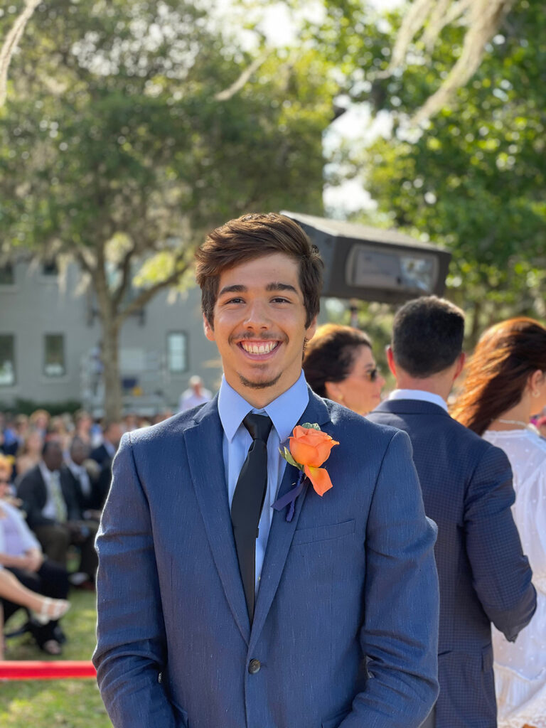 Caio Cavarsan, an international student from Brazil, smiling in a blue suit and black tie with an orange rose boutonniere.