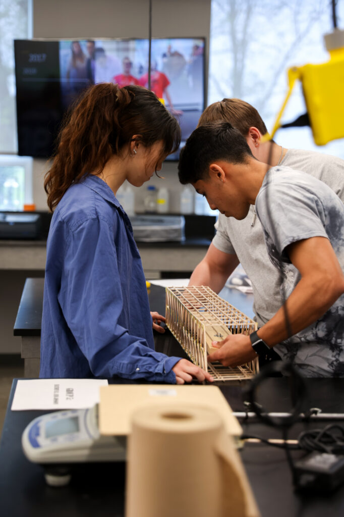 Engineering students collaborating over a balsa wood bridge model during a laboratory session.