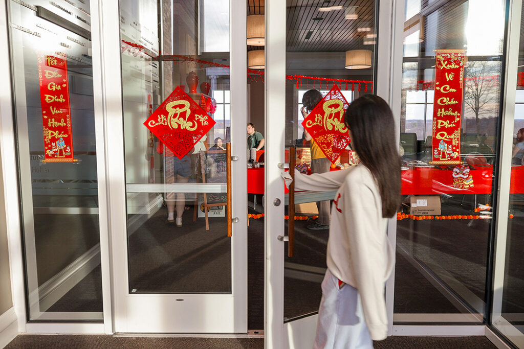 A student pushing open a glass door decorated with red Lunar New Year banners to enter a campus event.
