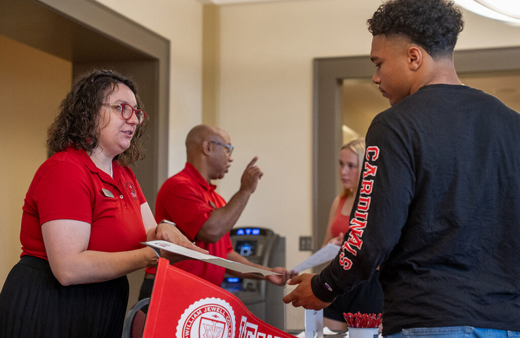 An admissions staff member handing registration materials to a prospective student at a Cardinal Day welcome table.