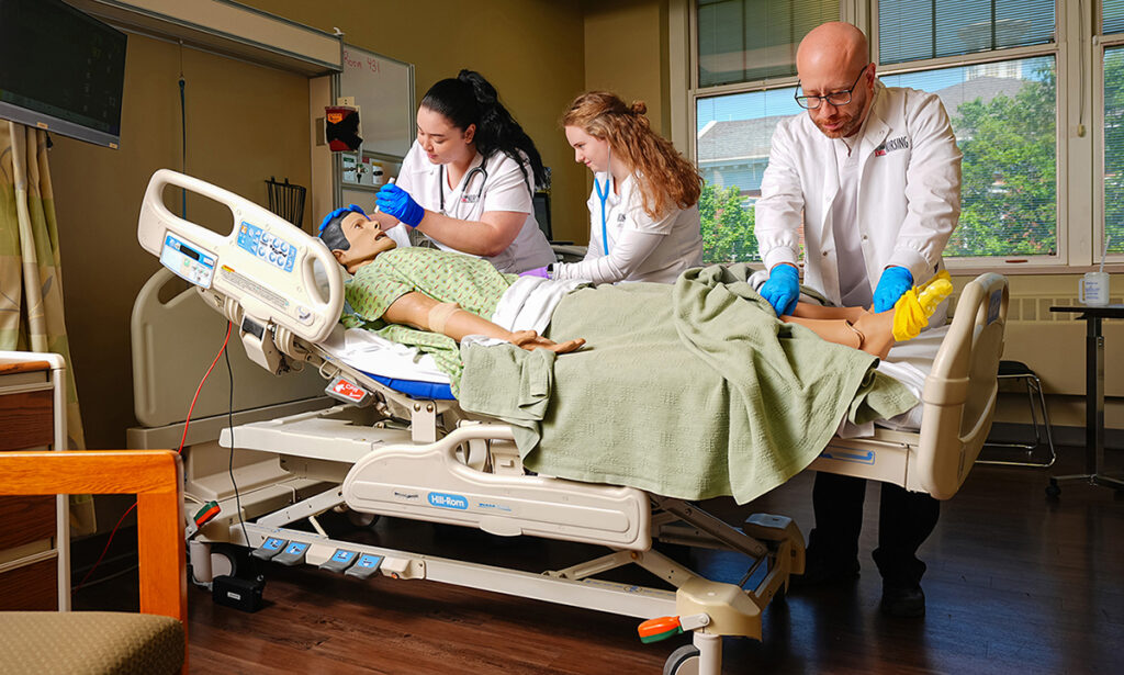 Nursing students and an instructor working together around a simulation mannequin in a medical training lab.