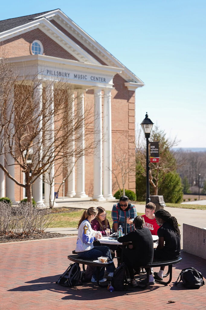 A group of students and an instructor studying around an outdoor table on campus in front of Pillsbury Music Center.