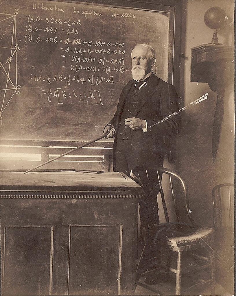 A professor holding a long pointer standing beside a blackboard filled with geometry formulas and a globe in a 1901 classroom.